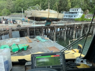 Damaged boat being lifted by crane on a dockside construction site with marine equipment in the Puget Sound region